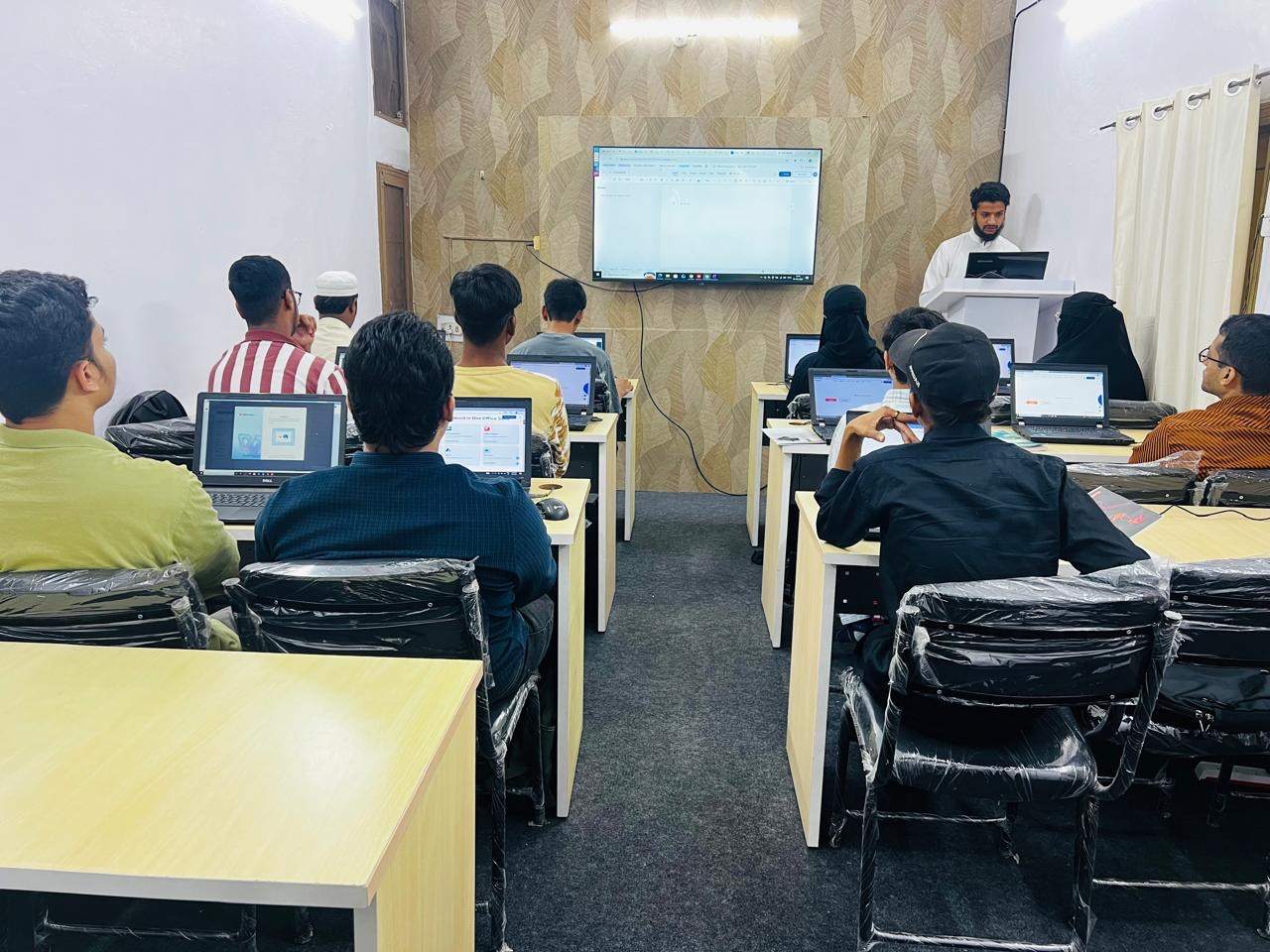 A NextGen session under way, learners at laptops facing the trainer and the screen